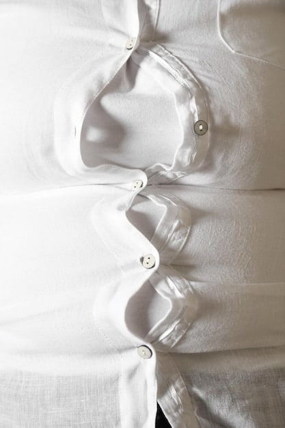 A close-up of a neatly folded white cotton shirt with a shallow depth of field, highlighting its crisp fabric and classic design.