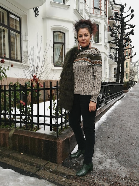 A woman wearing a stylish, oversized knit sweater paired with wide-leg corduroy pants in a muted earth tone, walking down a cobblestone street in a charming French village.