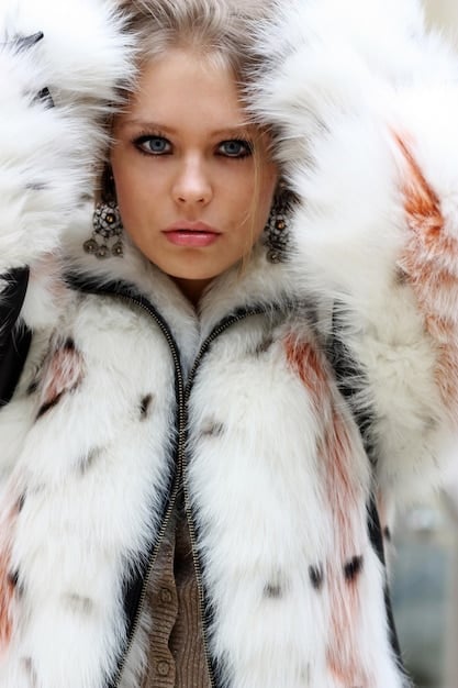 A close-up shot of a woman wearing a faux fur coat with a leopard print. She is also wearing a black turtleneck sweater and gold hoop earrings. The image focuses on the texture and details of the faux fur.