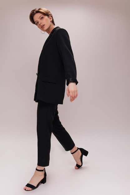 A full-length shot of a person wearing a stylish all-black monochrome outfit while walking down a city street. They are wearing a tailored coat, sleek trousers, and polished boots. The lighting is dim, creating a sophisticated and mysterious atmosphere.