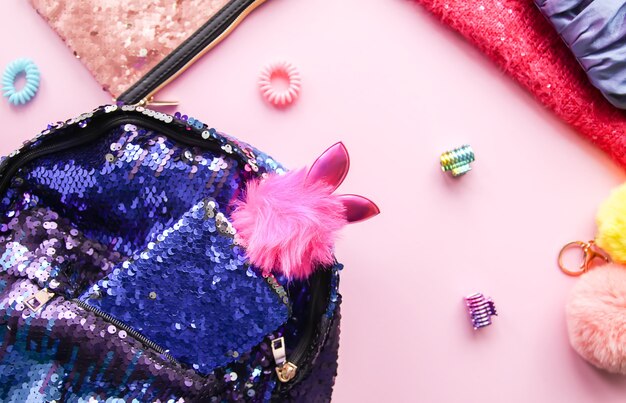 A close-up shot of Y2K accessories laid out on a pink velvet surface, including colorful plastic rings, butterfly hair clips, a baguette bag, and chunky platform sandals. The lighting is soft and creates a dreamy, nostalgic atmosphere.