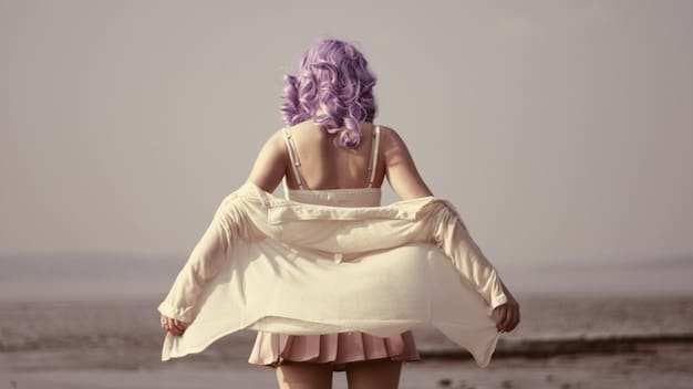 A model wearing a modern take on Y2K style: a silk slip dress paired with chunky sneakers, a denim jacket, and a minimalist chain necklace. The background is a clean, urban setting, emphasizing the blend of retro and contemporary elements.