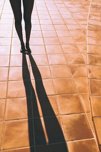 A close-up shot of a woman's lower body wearing a dark-wash flare jean with platform shoes, walking across a crosswalk. The focus is on the movement and the texture of the denim reflecting sunlight.