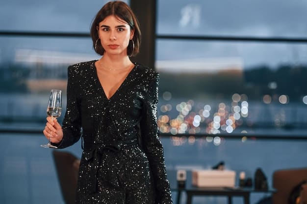 A woman at a cocktail party wearing a dark blue velvet oversized blazer over a sleek black jumpsuit. She is holding a champagne glass and wearing delicate silver jewelry.