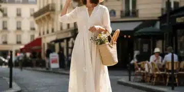Femme élégante en robe d'été légère, chapeau de paille et espadrilles, marchant dans une rue parisienne ensoleillée, incarnant le style français estival.